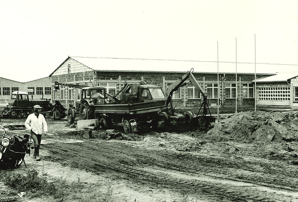 historie_bild_2_schwanteland_bauarbeiten_perewenitzer_chaussee Bauarbeiten mit mehreren Baufahrzeugen und einem Mann neben einem Pferd vor einem langgestreckten Industriegebäude.