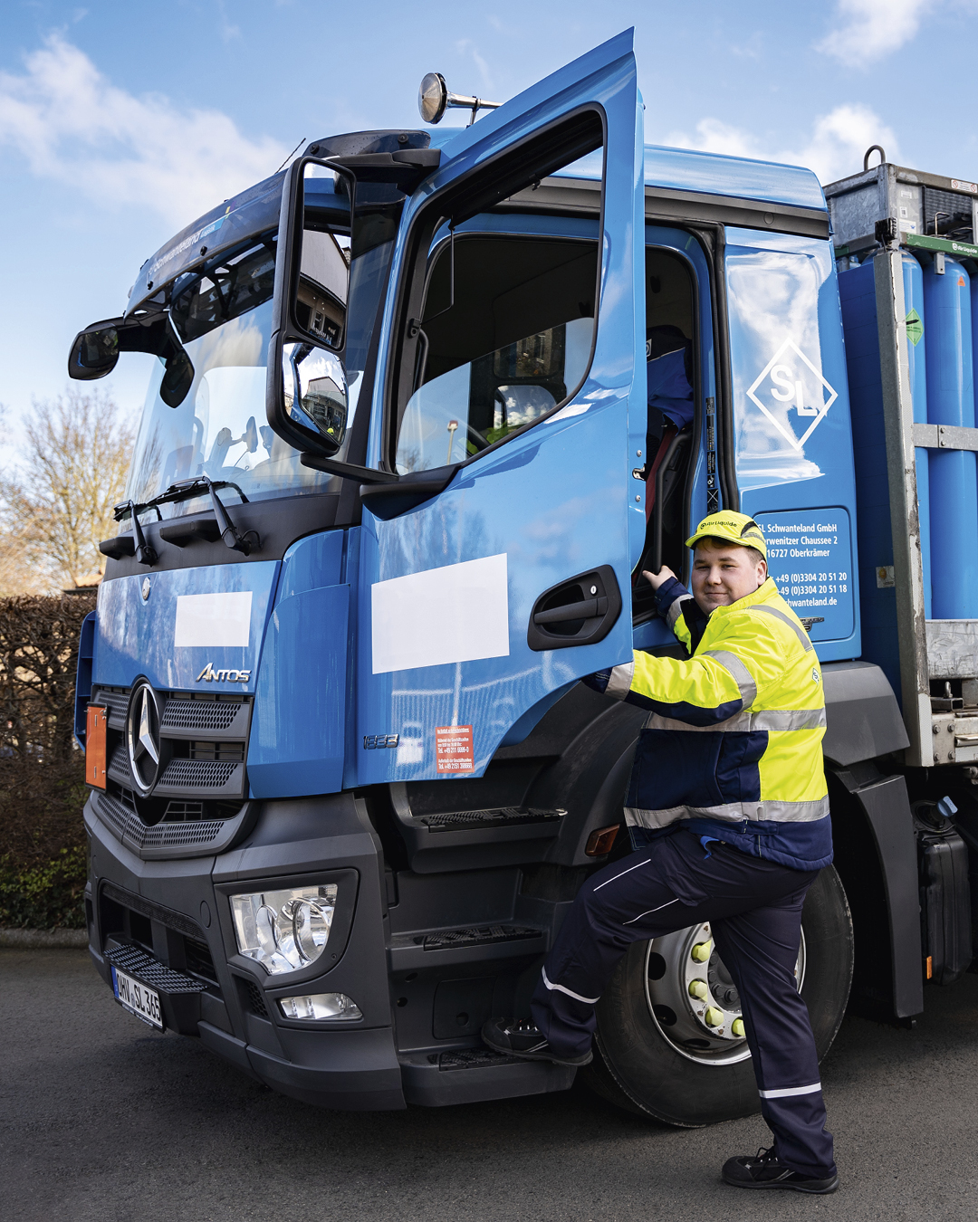 Blauer Mercedes-Lkw mit geöffneter Fahrertür, davor steht eine Person in gelb-blauer Warnschutzkleidung und steigt ein.